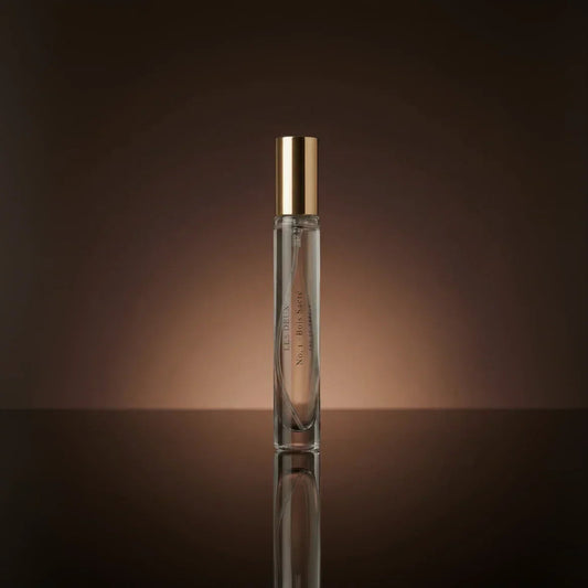 Perfume bottle with gold cap on a reflective surface and brown background