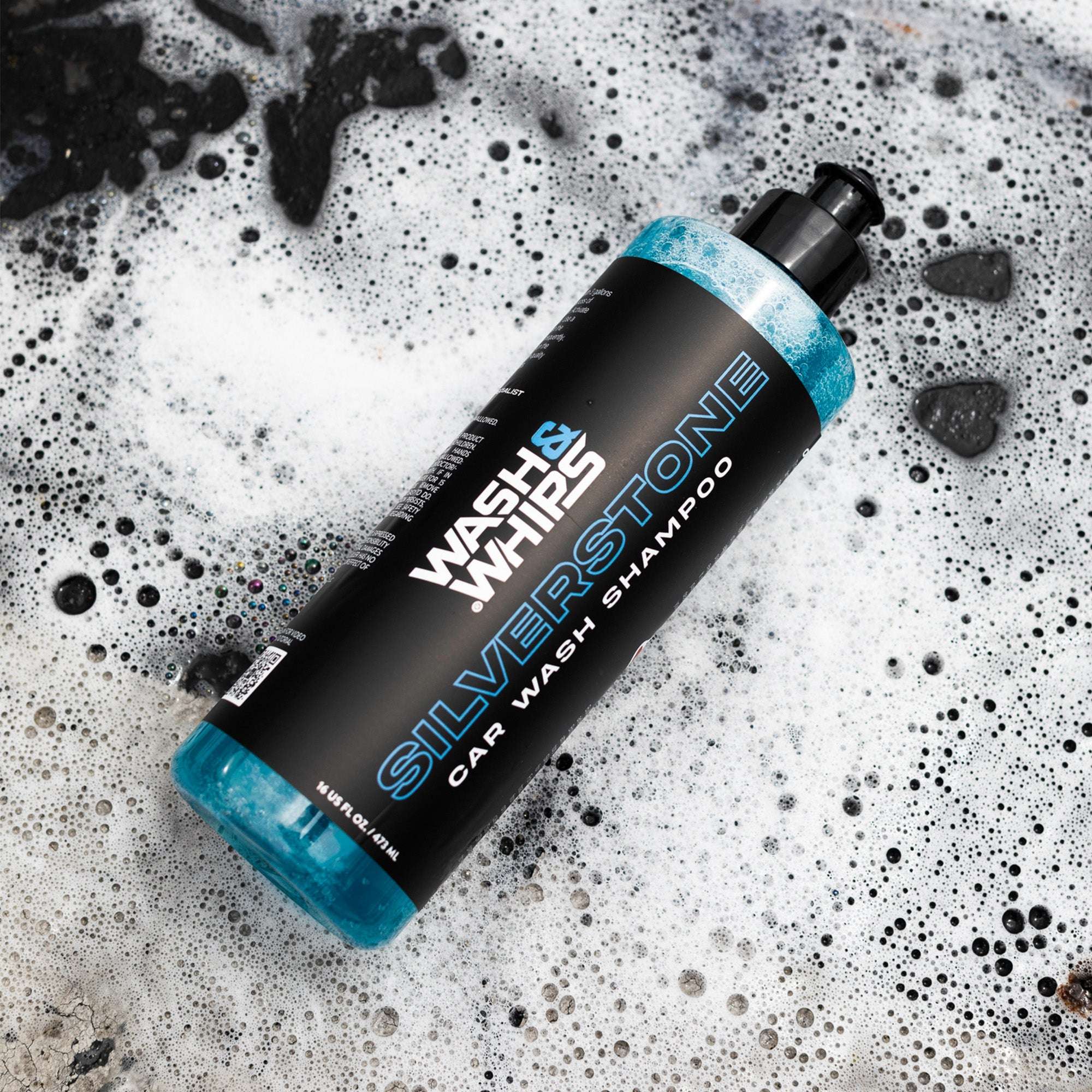 Bottle of Silverstone car wash shampoo on a textured surface with soap suds.