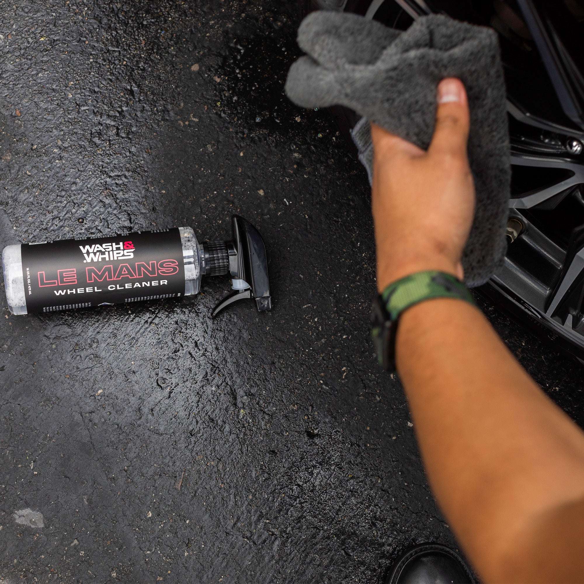 Hand holding a gray sponge next to a tube of Wheel Cleaner on a dark surface