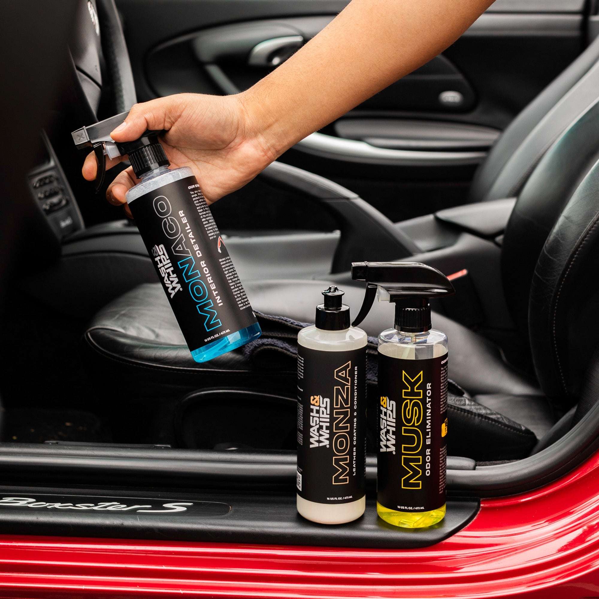 Person holding a bottle of car care product inside a car with additional bottles displayed.
