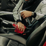Person cleaning car interior with a bottle of detailing product and a red cloth.