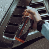 Hand holding a bottle of Hockenheim insect remover against a car vent.