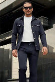 Man wearing a navy jacket, white shirt, and dark pants standing outdoors.