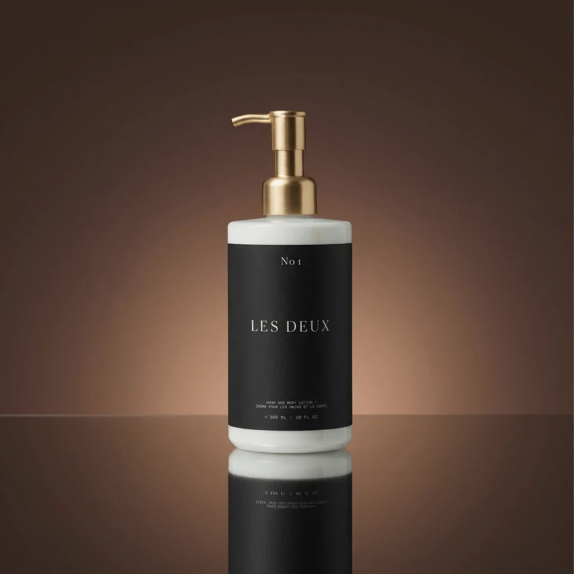 Bottle of 'Les Deux' with a gold pump on a reflective surface and brown background