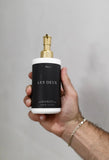 Hand holding a 'Les Deux' bottle with a gold pump against a gray background