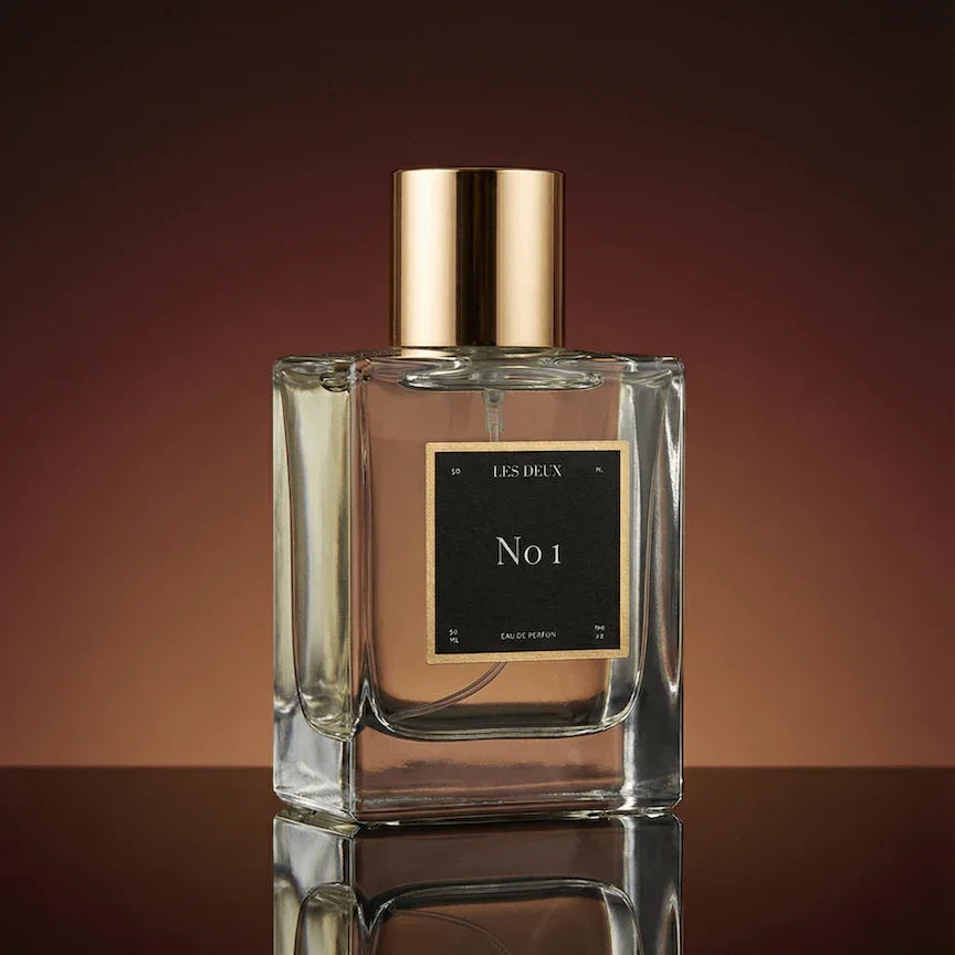 Perfume bottle with gold cap and 'No 1' label on a reflective surface with a gradient background