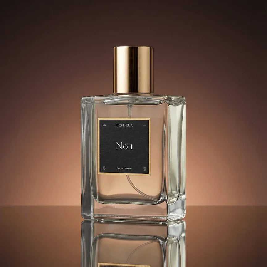 Perfume bottle with gold cap and black label on a reflective surface with a brown gradient background
