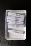 White rectangular dish with 'LES DEUX' branded items on a dark background