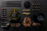 Two perfume bottles with dried leaves, flowers, and candles on a dark surface