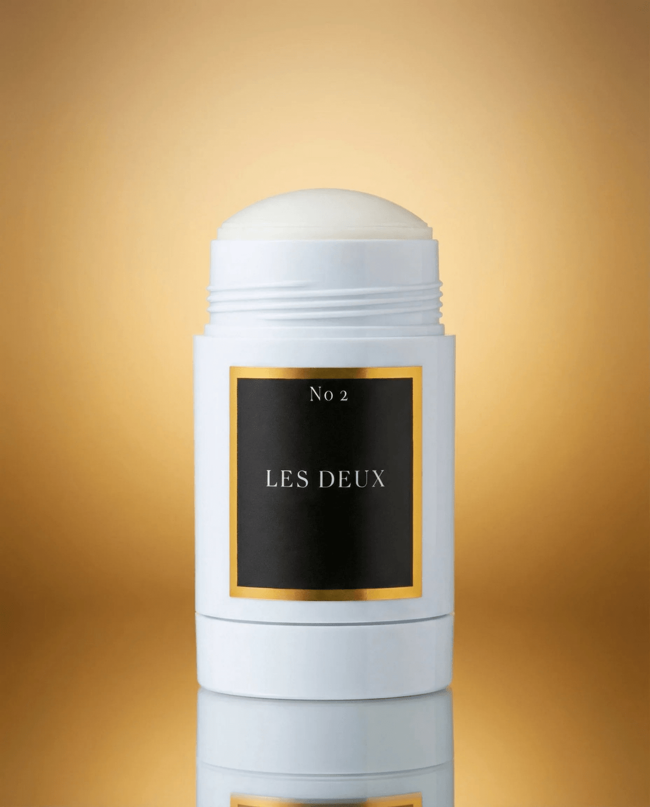 White deodorant stick with 'Les Deux' branding on a gold gradient background