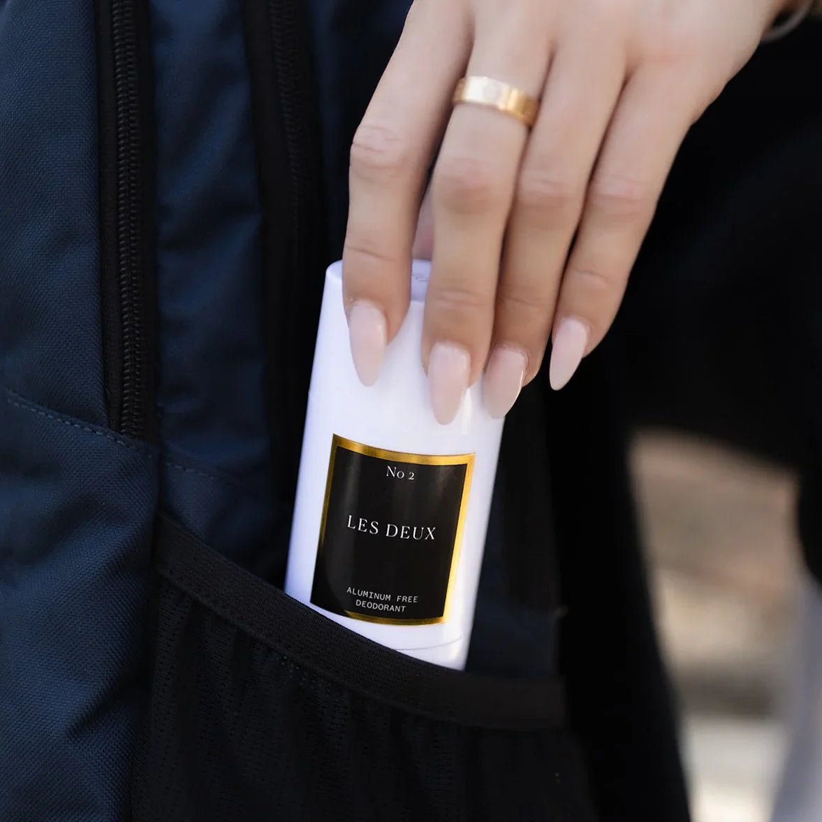 Hand holding a 'Les Deux' deodorant stick with a blurred background