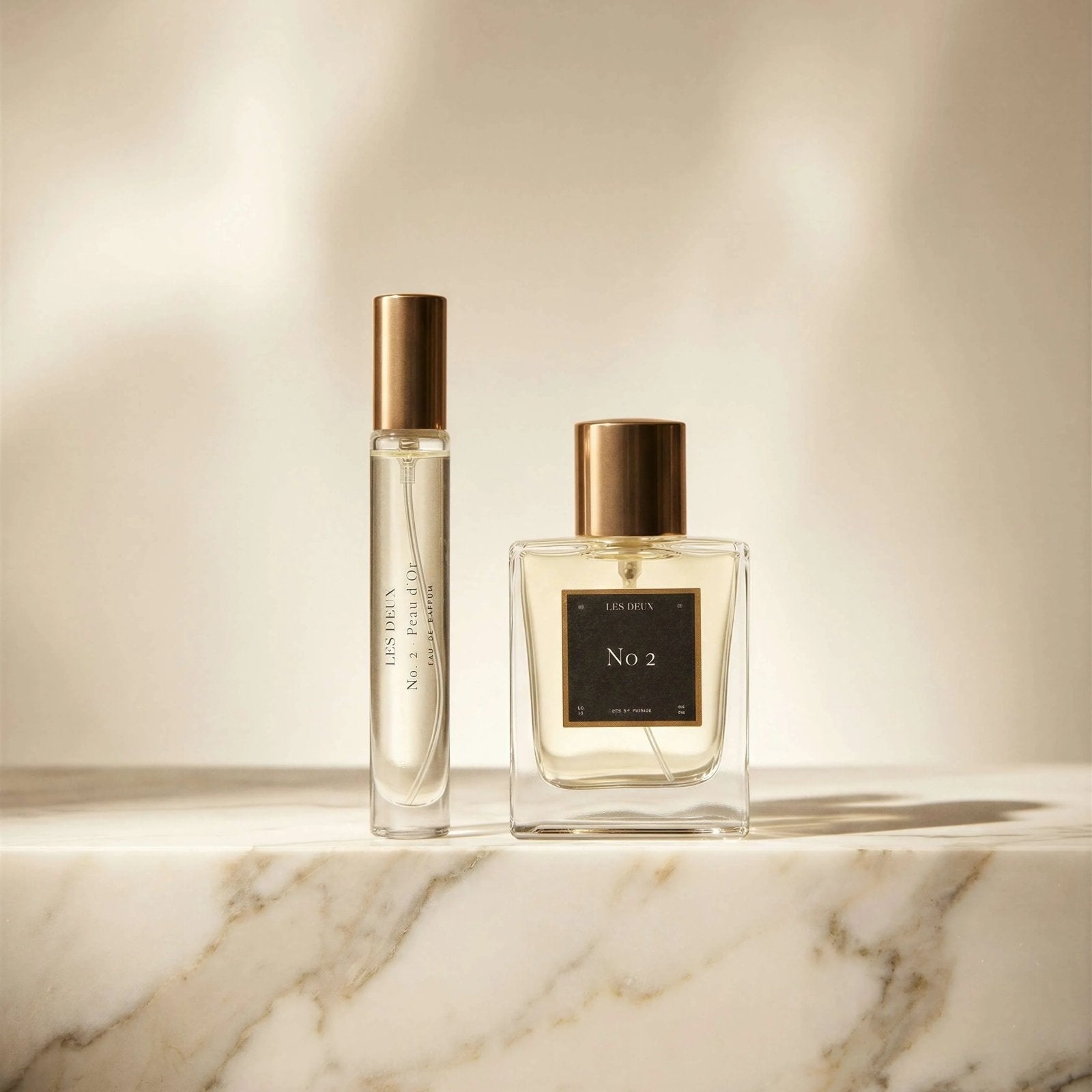Two perfume bottles on a marble surface with a neutral background