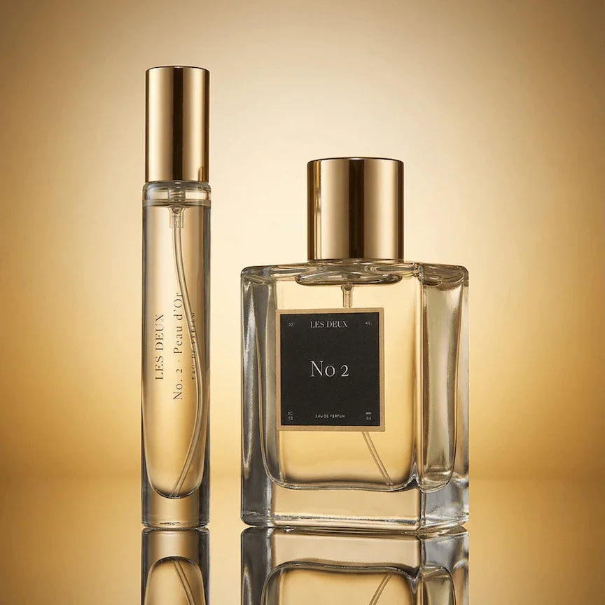 Two perfume bottles labeled 'No 2' on a reflective gold surface with a gradient background.