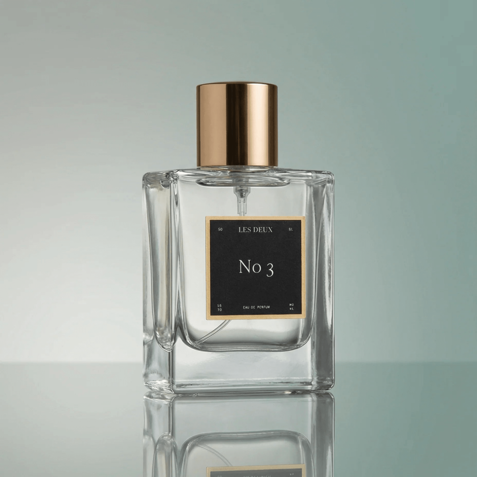 Clear perfume bottle with gold cap and black label on a reflective surface