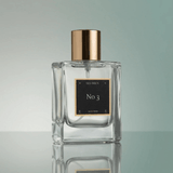 Clear perfume bottle with gold cap and black label on a reflective surface
