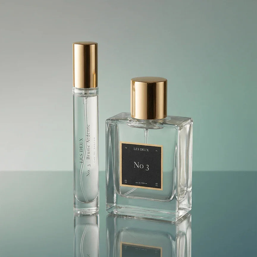 Two perfume bottles with gold caps on a reflective surface with a gradient background