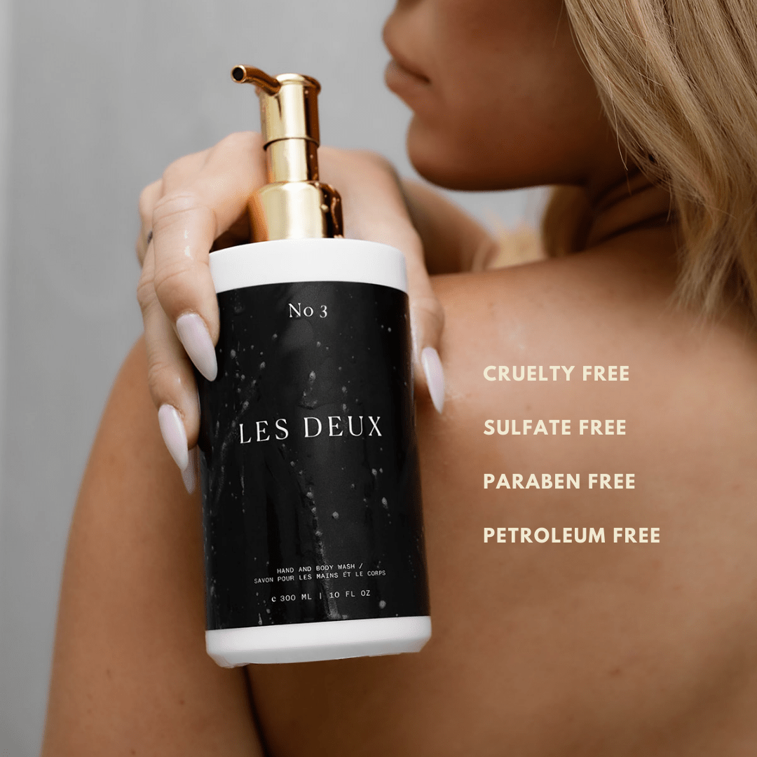 Person holding a bottle of 'Les Deux' skincare product with product details on a gray background