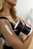 Person applying a black and gold bottle of 'LES DEUX' body lotion to their arm.
