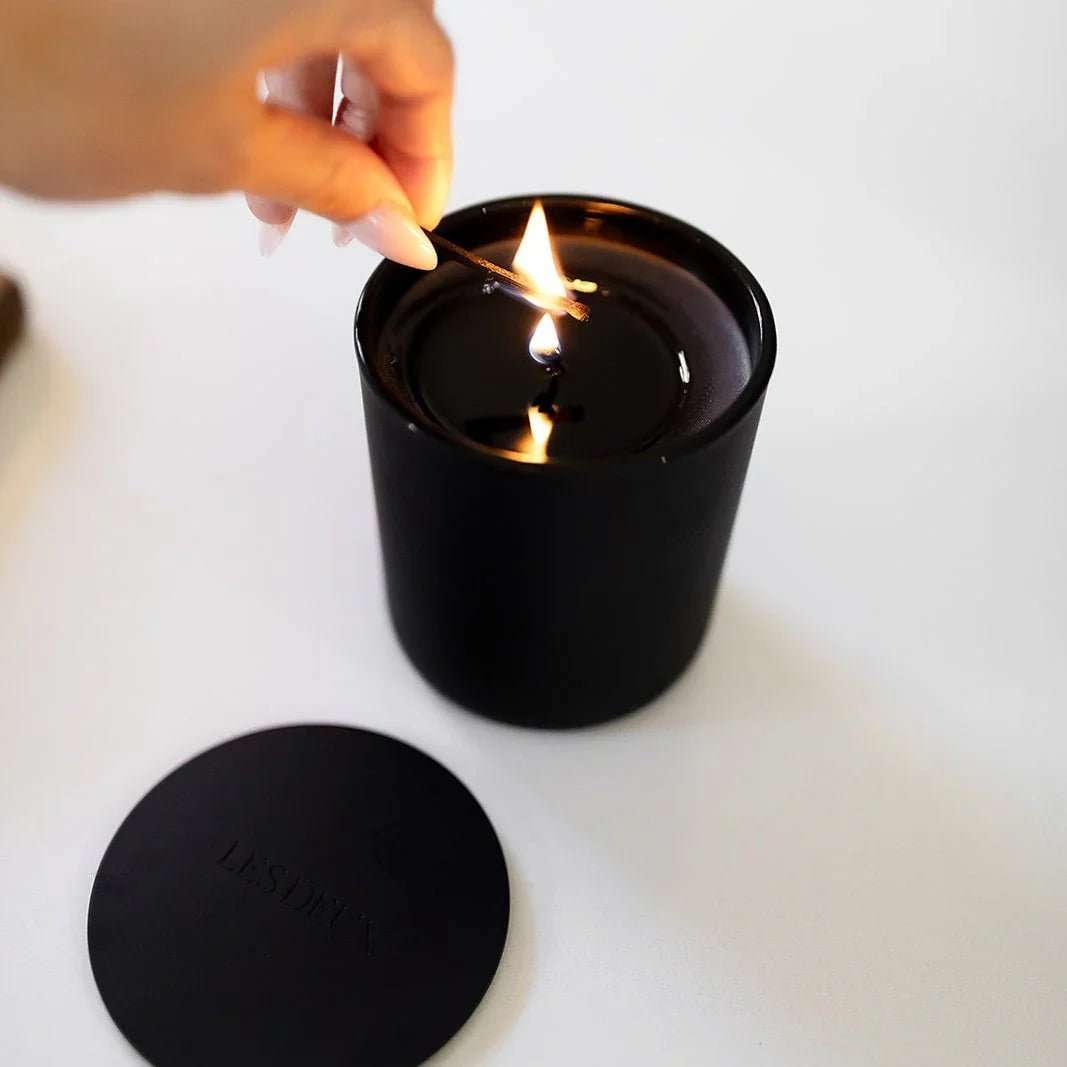 Person lighting a black candle with a matching lid on a white surface