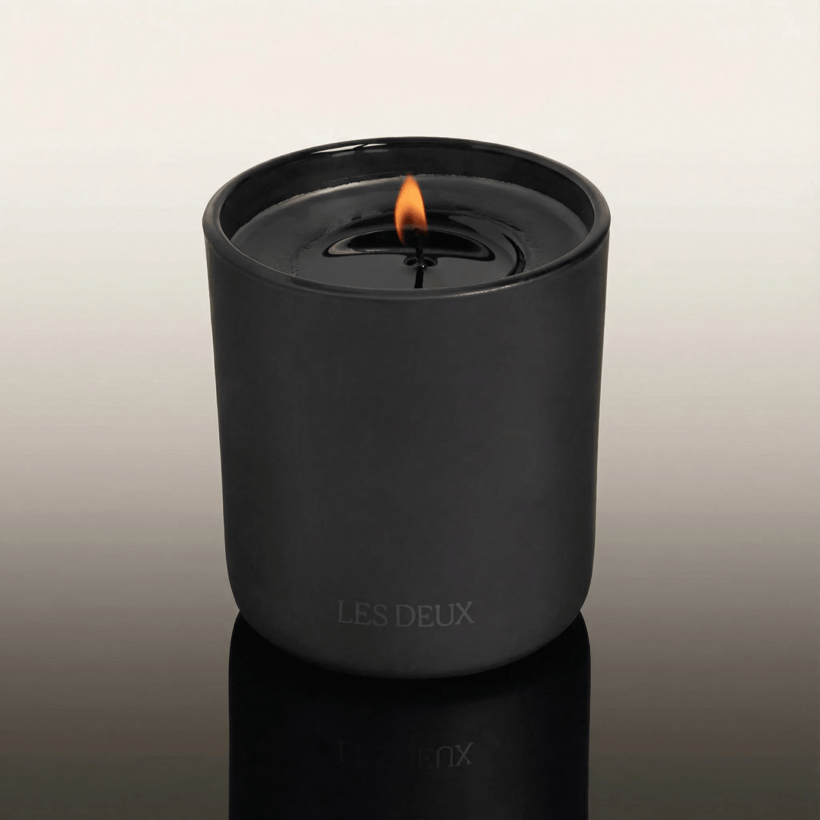 Black candle in a container with 'LES DEUX' branding on a reflective surface.