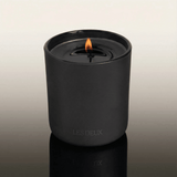 Black candle in a container with 'LES DEUX' branding on a reflective surface.