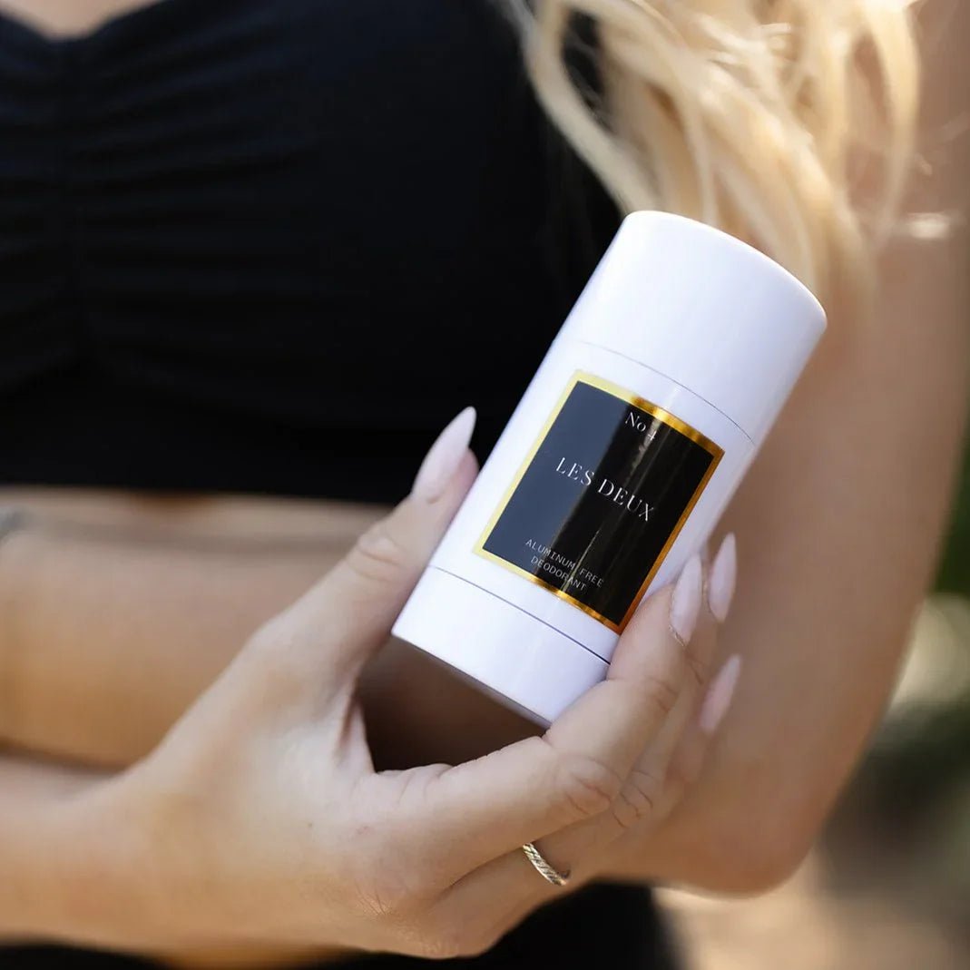 Hand holding a white container with 'Les Deux' branding against a blurred background