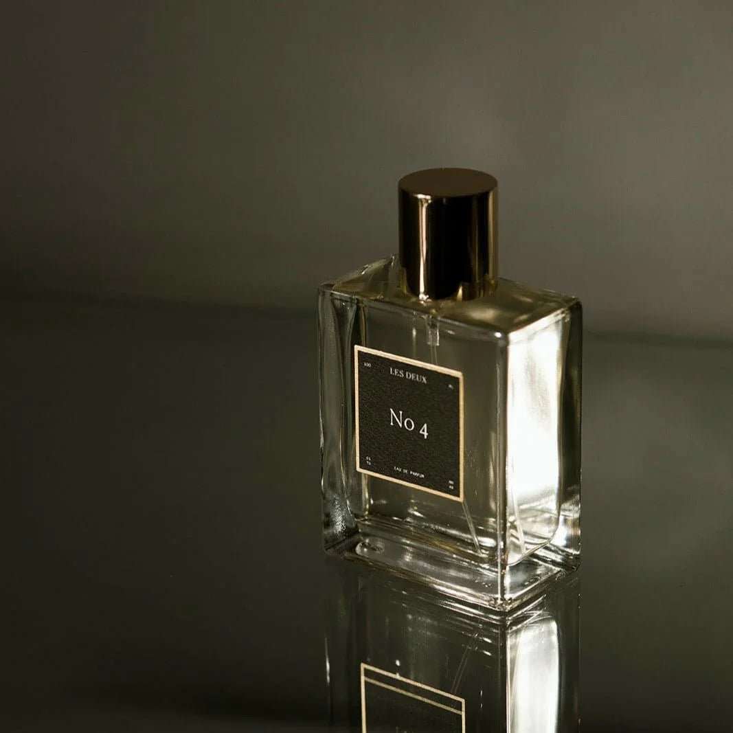 Glass perfume bottle with gold cap and label on a reflective surface
