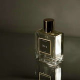 Glass perfume bottle with gold cap and label on a reflective surface
