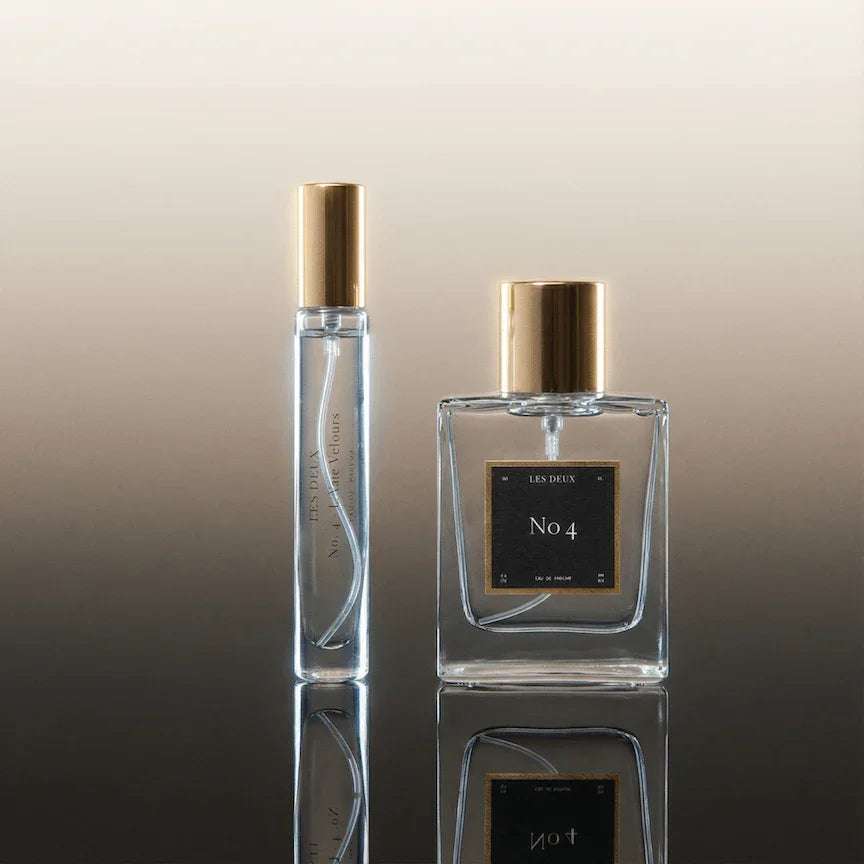 Two perfume bottles with gold caps on a reflective surface with a gradient background