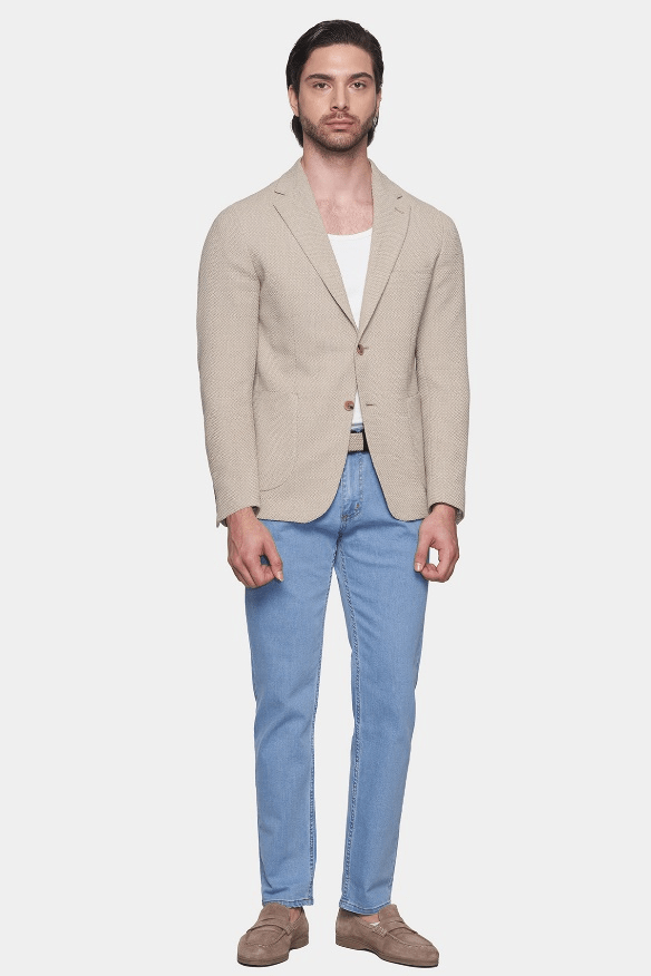 Man wearing a beige blazer, white shirt, and blue jeans on a white background