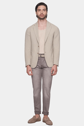 Man wearing a beige blazer, beige shirt, and gray pants on a white background