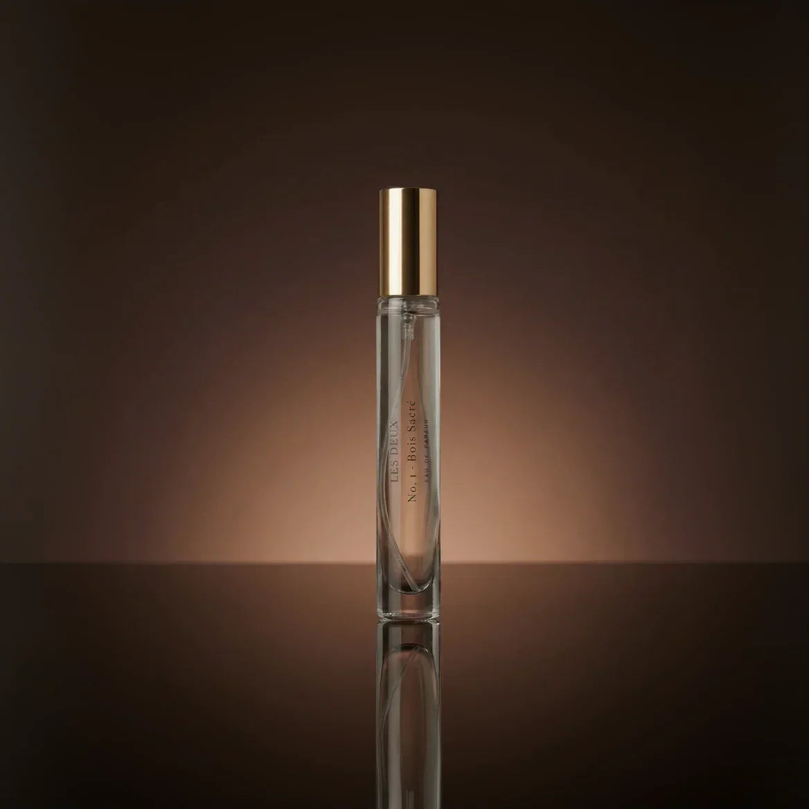 Perfume bottle with gold cap on a reflective surface and brown background